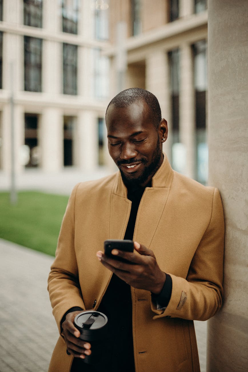 selective focus photo of smiling man looking at his phone while holding cup